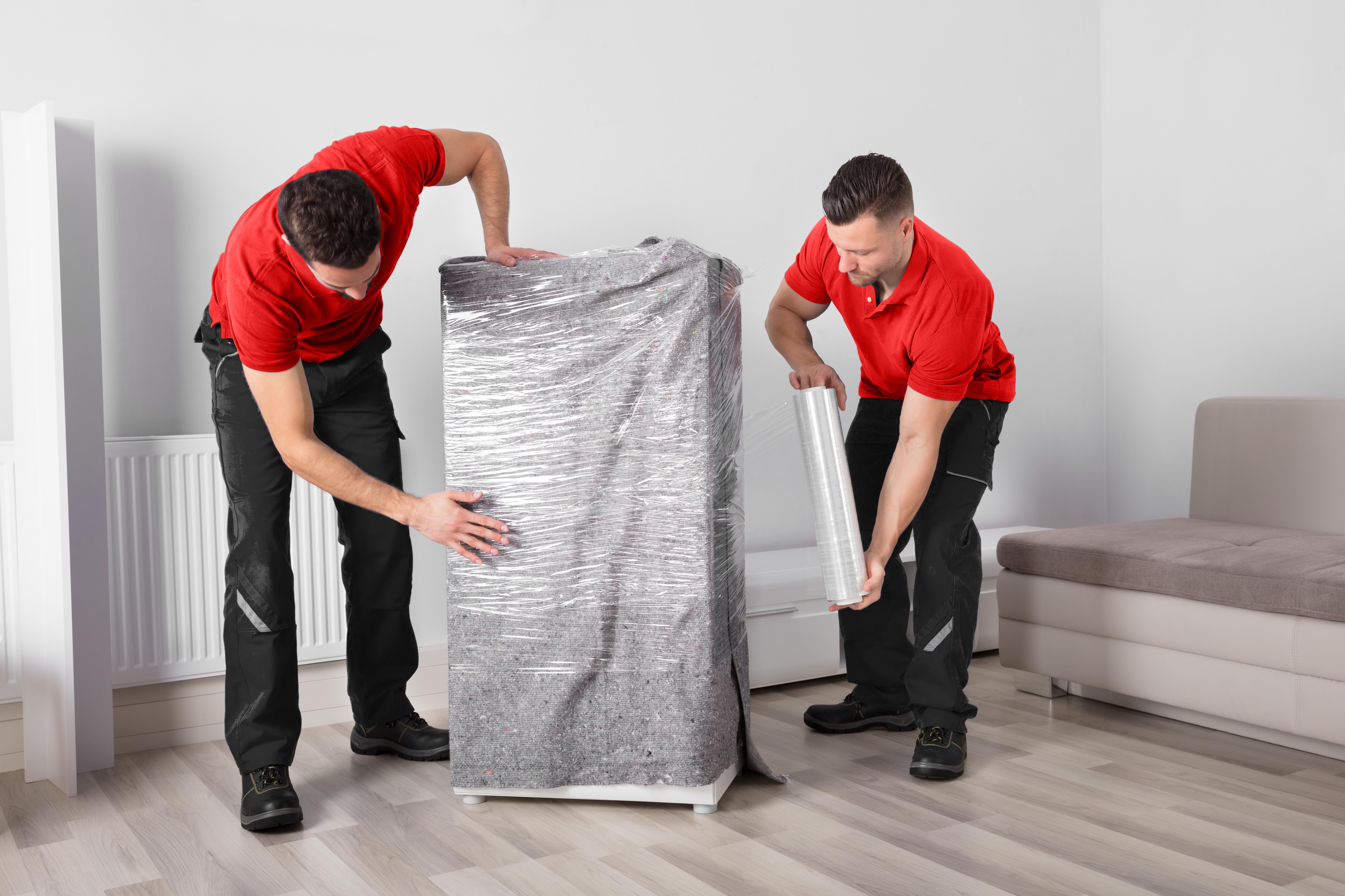 Two movers wrapping office equipment in protective plastic wrap